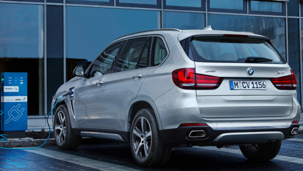 A silver BMW X5 is plugged into an electric charging station in front of a modern building, 4K Desktop Wallpaper