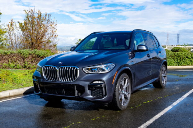 A sleek BMW X5 is parked on a wet pavement with trees and a cloudy sky in the background, HD Desktop Wallpaper