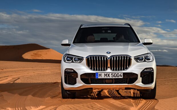A white BMW X5 is parked on sandy desert terrain under a cloudy sky, 2K Desktop Wallpaper