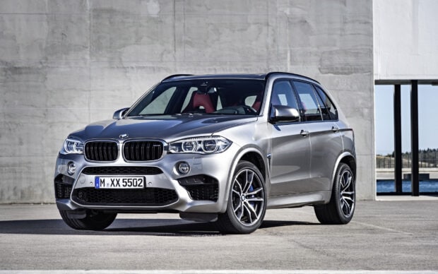 A silver BMW X5 is parked on an open concrete area near a modern building, showcasing its sporty design