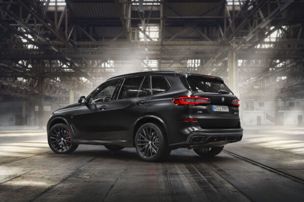 A black BMW X5 is parked inside a spacious industrial warehouse with beams and high windows, HD Desktop Wallpaper