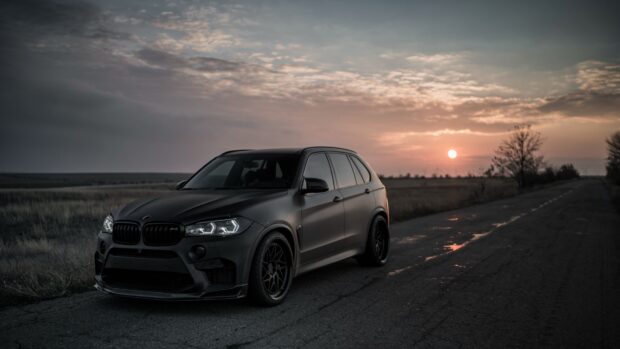 A black BMW X5 is parked on a quiet rural road under a dramatic sunset sky, 4K Desktop Wallpaper