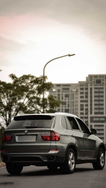A BMW X5 is parked on a city street with buildings and trees in the background, 2K Phone Wallpaper