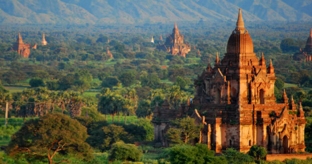 Ancient temples of Bagan surrounded by lush greenery and distant mountains at sunset