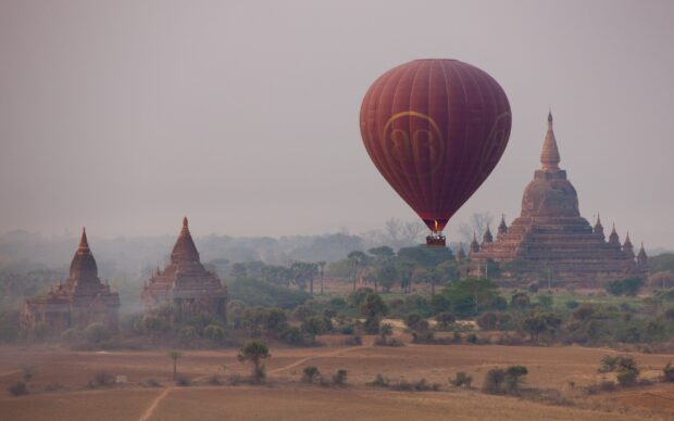 A hot air balloon flying over ancient Bagan temples in a misty landscape