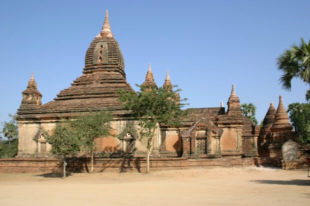 Ancient Bagan temple surrounded by trees under clear blue sky