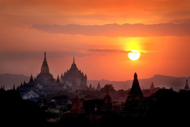 Ancient Bagan temples silhouetted against a vibrant sunset sky with the sun glowing brightly