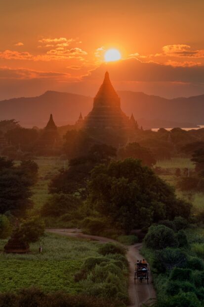 A scenic view of Bagan temples at sunset with a horse carriage on a dirt road