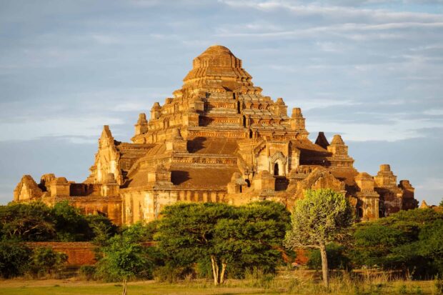 Ancient temple structure in Bagan surrounded by green trees under a cloudy sky