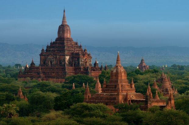 Ancient Bagan temple surrounded by lush greenery and distant mountains at dusk