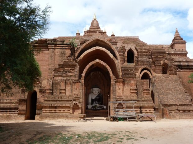 Ancient Bagan temple with a large Buddha statue inside the brick archway surrounded by trees