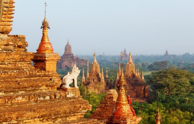 Ancient Bagan temples with lion statue and distant pagodas in a vast green landscape