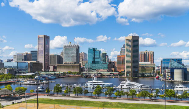 Baltimore skyline with modern tall buildings and boats on the harbor under a bright blue sky