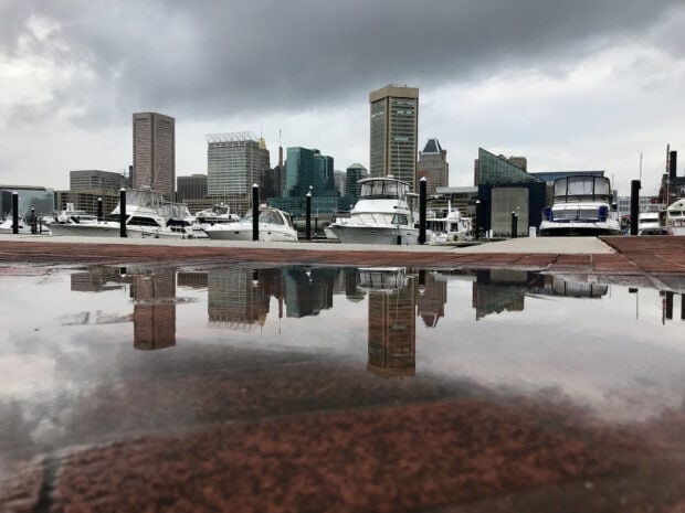 Baltimore skyline reflected in a puddle near a marina with boats and cloudy sky