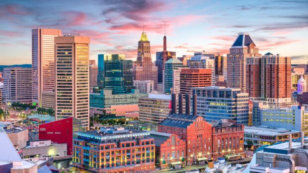 The Baltimore skyline features iconic buildings under a colorful sunset sky