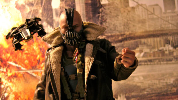 Bane character from Batman standing with a clenched fist in front of an explosion