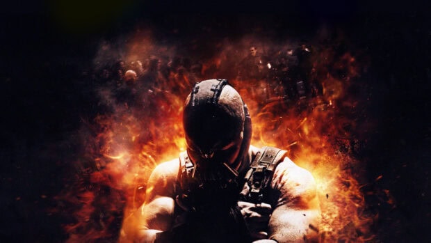 Bane character from Batman standing amid fiery explosion with crossed arms