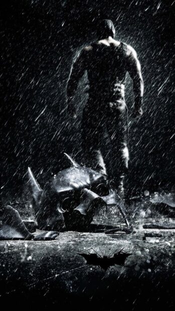 Bane stands in the rain with the broken Batman mask on the ground before him