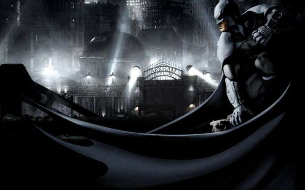 Batman Arkham City features Batman perched in front of the Arkham Asylum gate at night