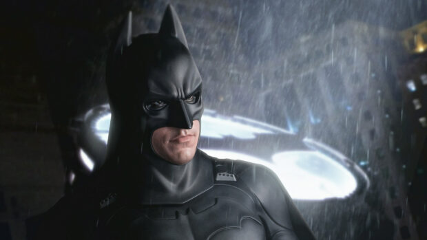 Batman begins character standing in the rain with the bat symbol glowing in the background