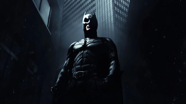 Batman begins character standing in a dark city with tall buildings behind him