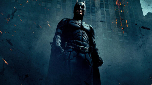 Batman Begins character standing in front of a burning building in a dark cityscape