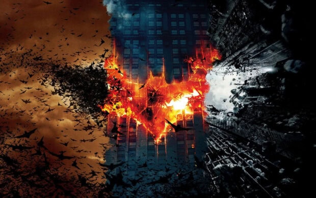 A flaming bat symbol formed by bats flying in front of city buildings at dusk