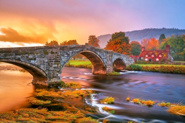 A stone bridge over a flowing river with autumn trees in Wales, HD Desktop Wallpaper