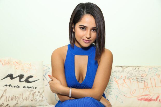 Becky G wearing a blue dress sitting on a graffiti covered couch