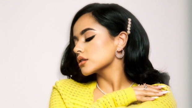 Becky G wearing yellow textured top and pearl jewelry with eyes closed