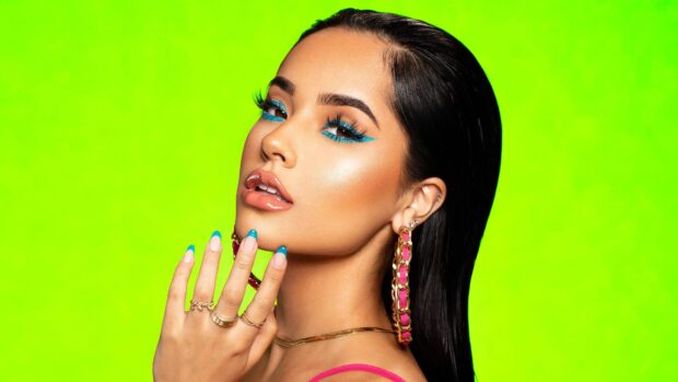 Becky G wearing large hoop earrings and blue eye makeup on a bright green background