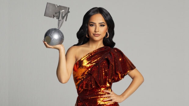 Becky G wearing a shiny red dress holding an MTV award in one hand