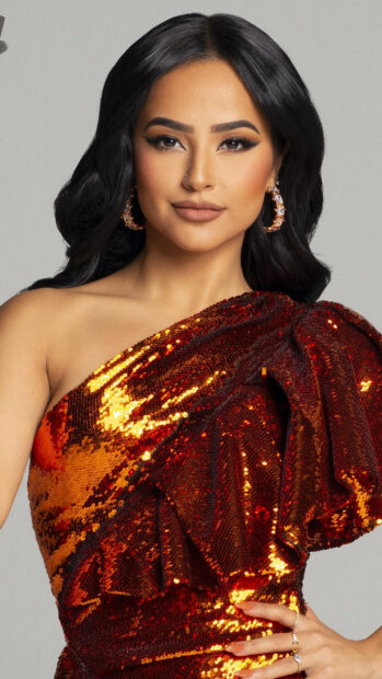 Becky G wearing a shiny orange dress with sequins and hoop earrings looking confidently at the camera