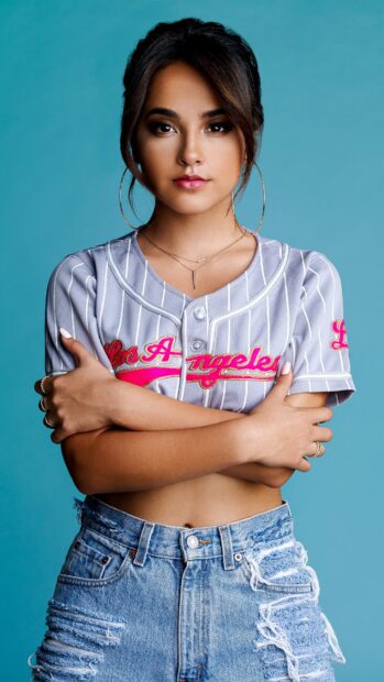 Becky G posing confidently in casual outfit with crossed arms on blue background