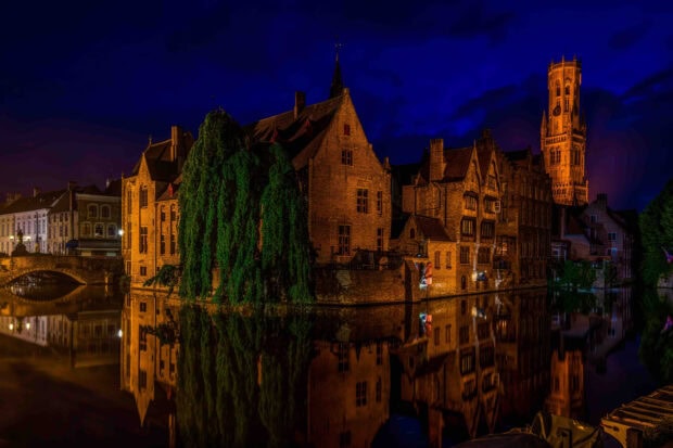 Historic Belgium architecture reflected in the canal at night with a deep blue sky