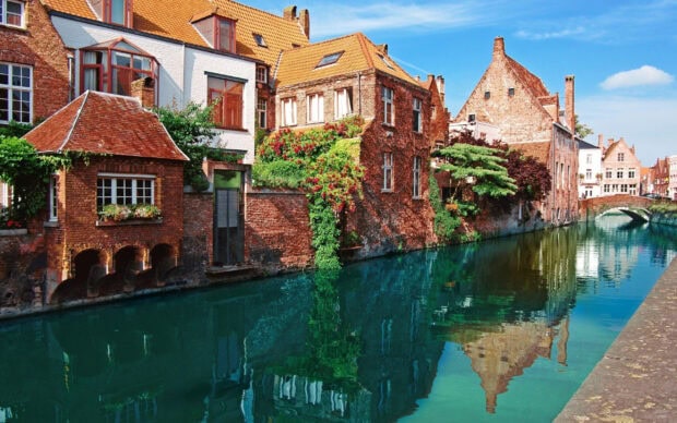 Historic Belgium architecture with canal reflections and vibrant greenery