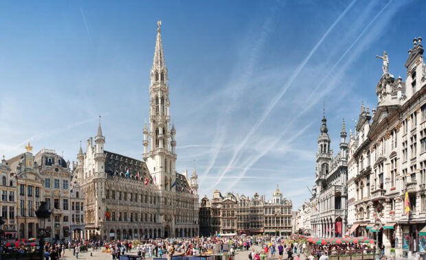 Historic Belgium architecture with a large crowd gathered in a city square under a clear blue sky