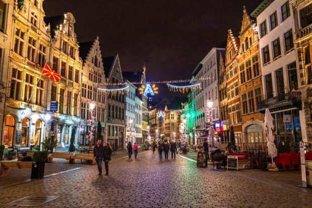 Night street in Belgium with historic buildings and people walking on cobblestone path