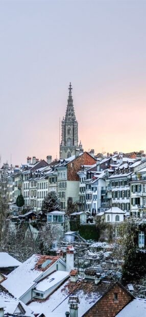 Snow covered houses and historic cathedral tower in Bern Switzerland at sunset