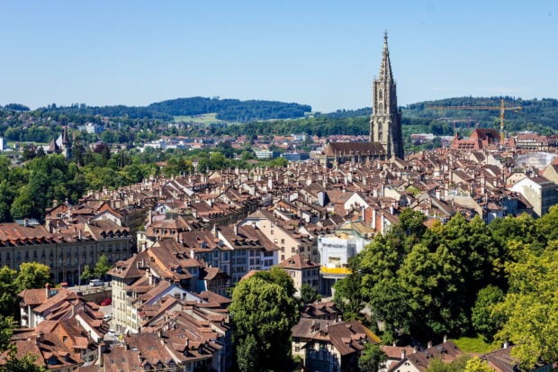 A panoramic view of Bern Switzerland cityscape with historic buildings and a cathedral tower under clear blue sky