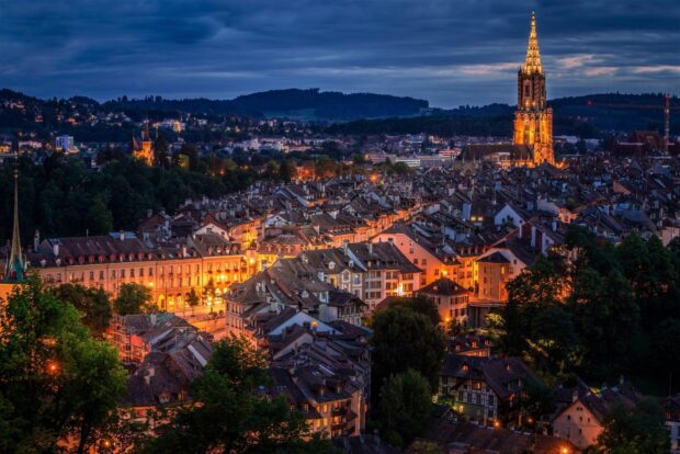 Bern Switzerland Wallpaper showcasing the illuminated city skyline at dusk with historic buildings and church towers