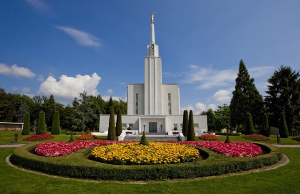 Beautiful white building with colorful flower garden and green trees under blue sky in Bern Switzerland