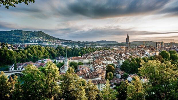Bern Switzerland cityscape with historic buildings and lush green trees under a cloudy sky