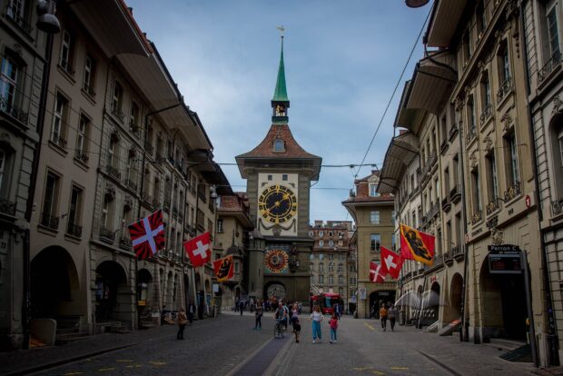 A historical clock tower and flags line a cobblestone street in Bern Switzerland wallpapers