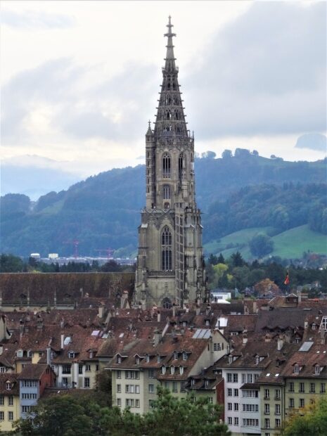 A tall historic cathedral tower rises above rooftops in Bern Switzerland against misty hills