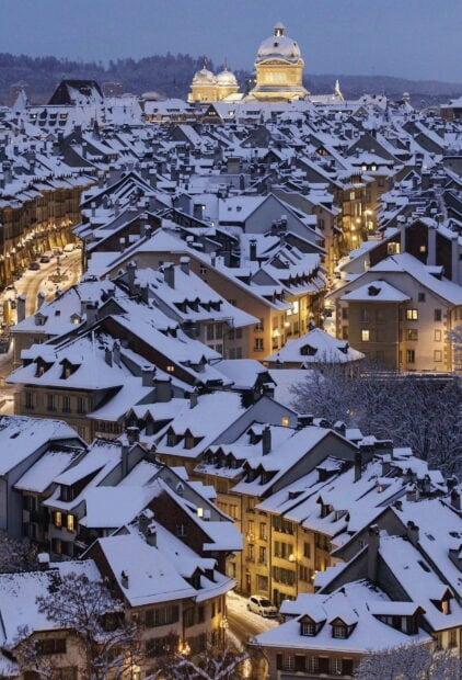 Bern Switzerland cityscape covered with snow at dusk showing historic buildings and glowing streetlights
