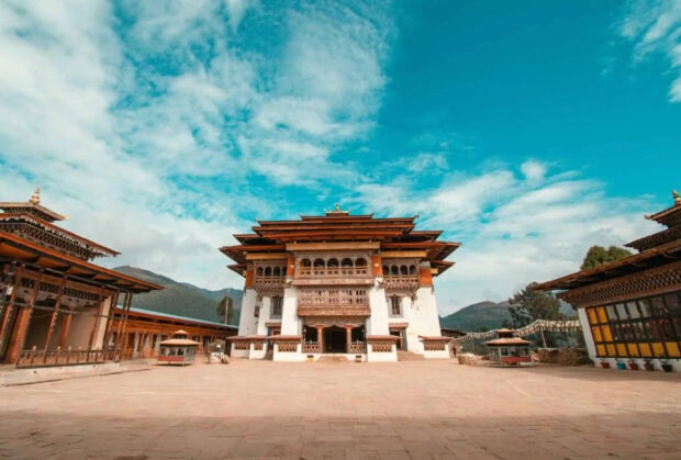 Traditional Bhutan architecture under a bright blue sky surrounded by mountains