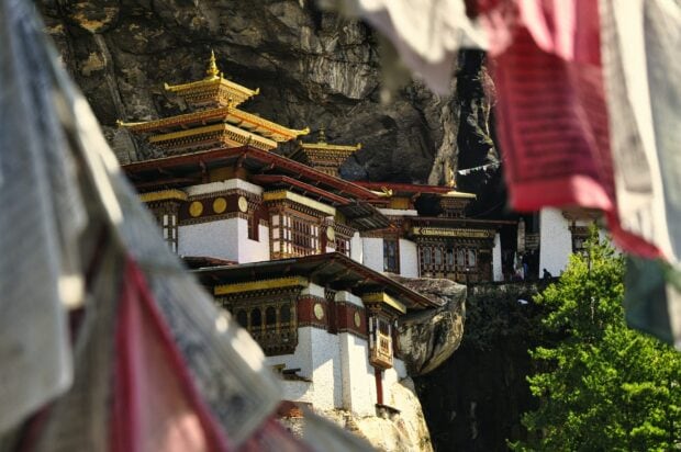 Ancient Bhutan architecture built into a rocky cliff surrounded by prayer flags and greenery