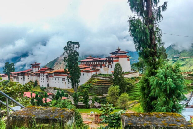 Traditional Bhutan fort surrounded by lush green landscape and misty mountains in Bhutan