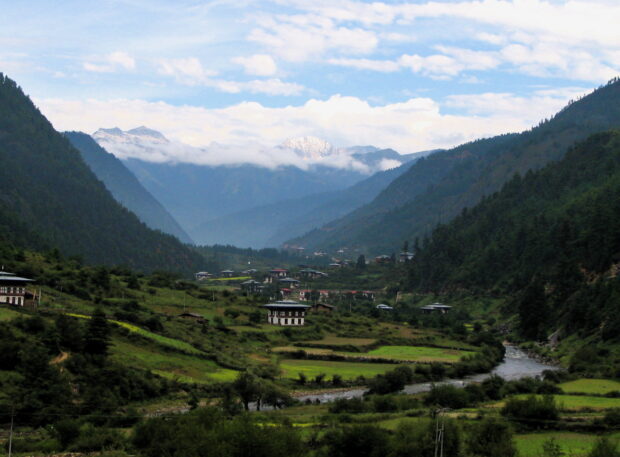 Traditional Bhutanese village nestled in lush green valley surrounded by mountains in Bhutan